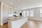 Located at 1035 Bexley Square in Chattanooga, Tennessee, this single-floor residence combines modern finishes with a clean, open layout. The heart of the home is a spacious open-concept living and kitchen area bathed in natural light from multiple windows dressed with white blinds. The kitchen is a standout, featuring grey shaker-style cabinetry, a white subway tile backsplash, granite countertops, and a full suite of stainless steel appliances including a refrigerator, range, and microwave. A large kitchen island with a granite top and integrated sink serves as both a functional workspace and a natural gathering point. Light-toned hardwood-style flooring runs seamlessly throughout the entire space, creating a cohesive and airy feel. The bedroom is generously sized with ample natural light and direct access to a walk-in closet with built-in shelving and hanging rods. A secondary closet offers additional storage. The primary bathroom includes a glass-enclosed shower, a granite-topped vanity with grey cabinetry, and clean, neutral finishes. A second bathroom features a tub-shower combination. Additional storage is provided by a well-organized pantry or utility closet fitted with wire shelving. The overall aesthetic is bright, contemporary, and move-in ready.
