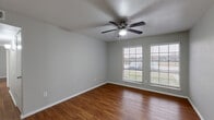 Located at 1002 S Edmonds Ln in Lewisville, TX, this single-story 2-bedroom, 2-bathroom home offers a practical and comfortable layout. Warm-toned wood-look flooring runs consistently throughout the living areas and bedrooms, contributing to a cohesive and inviting aesthetic. Neutral gray walls complement the flooring and provide a versatile backdrop throughout the space.

The combined kitchen and living room area forms the heart of the home. The kitchen features white cabinetry, granite-look countertops, black appliances including a range, microwave, and dishwasher, and a decorative tile backsplash that adds visual interest. The adjacent living area is brightened by a ceiling fan with a light fixture and offers access to the front entry door.

The spacious primary bedroom includes two windows with blinds that allow natural light, a ceiling fan, and a closet. A dedicated vanity area with a granite-look countertop, large mirror, and Hollywood-style lighting serves the primary bath, which also includes a tub-shower combination. The second bedroom is well-sized, also featuring a ceiling fan, a closet, and a window. Two closets throughout the home provide ample storage. Textured ceilings are present in select rooms, adding a classic touch to the overall design.