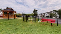 Located in Conyers, GA, this residential community offers a well-maintained outdoor environment designed with both residents and their pets in mind. The grounds feature a dedicated, fenced dog park enclosed by black chain-link fencing, equipped with pet agility elements including a tunnel obstacle and a secured entry gate. A red bench positioned alongside the park provides a comfortable spot for owners to supervise their pets. Lush green lawns surround the area, contributing to an open and welcoming atmosphere.

A charming wooden gazebo with a pitched roof anchors one end of the outdoor space, offering a shaded gathering area complemented by decorative lamp posts and mature trees that provide additional canopy. Views of the surrounding multi-story residential buildings are visible throughout, framed by well-kept landscaping and ample parking areas.

The covered exterior corridors feature white vinyl siding, concrete flooring, and black metal staircases with iron railings—providing residents with sheltered access between floors and units. Unit entryways along the corridor are fitted with classic black paneled doors. The overall community presents a clean, functional, and pet-friendly design suited for comfortable residential living in the greater Atlanta metro area.
