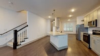 Located at 2789 Satellite Blvd in Duluth, GA, this well-appointed two-story residence offers three bedrooms and two and a half bathrooms across a generously sized floor plan. The main level showcases an open-concept layout where the kitchen flows seamlessly into the living area, all unified by rich, dark hardwood-style flooring. The kitchen is a standout feature, boasting gray shaker cabinetry, granite countertops, a central island with pendant lighting, a subway tile backsplash, and a full suite of stainless steel appliances including a French door refrigerator, electric range, built-in microwave, and dishwasher. Natural light filters in through large windows fitted with blinds, brightening the open living space. A staircase with a dark wood newel post and white balusters leads to the upper level, where the bedrooms are situated. The primary suite includes an en-suite bathroom featuring a dual-sink vanity with granite countertops, gray cabinetry, and a walk-in glass shower with white tile surround. Additional bedrooms are carpeted and well-lit with ceiling fans and windows. A dedicated upstairs laundry room with a full-size washer and dryer adds everyday convenience. The half bath completes the main floor. Clean white walls and modern finishes throughout give the home a bright, contemporary feel.