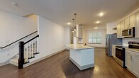 Located at 2789 Satellite Blvd in Duluth, GA, this well-appointed two-story residence offers three bedrooms and two and a half bathrooms across a generously sized floor plan. The main level showcases an open-concept layout where the kitchen flows seamlessly into the living area, all unified by rich, dark hardwood-style flooring. The kitchen is a standout feature, boasting gray shaker cabinetry, granite countertops, a central island with pendant lighting, a subway tile backsplash, and a full suite of stainless steel appliances including a French door refrigerator, electric range, built-in microwave, and dishwasher. Natural light filters in through large windows fitted with blinds, brightening the open living space. A staircase with a dark wood newel post and white balusters leads to the upper level, where the bedrooms are situated. The primary suite includes an en-suite bathroom featuring a dual-sink vanity with granite countertops, gray cabinetry, and a walk-in glass shower with white tile surround. Additional bedrooms are carpeted and well-lit with ceiling fans and windows. A dedicated upstairs laundry room with a full-size washer and dryer adds everyday convenience. The half bath completes the main floor. Clean white walls and modern finishes throughout give the home a bright, contemporary feel.