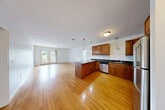 Located at 32 Carousel Ln in Lunenburg, MA, this 2-bedroom, 3-bathroom residence offers a thoughtfully designed single-floor layout with a generous amount of living space. The open-concept kitchen and living area serves as the heart of the home, featuring rich, warm-toned hardwood floors that extend throughout the main living spaces. The kitchen is well-appointed with rich wood cabinetry, dark granite countertops, a central island, pendant lighting, and a full suite of stainless steel appliances including a refrigerator, range, microwave, and dishwasher. The expansive living room is bathed in natural light and opens directly onto a private balcony through double French doors, offering pleasant outdoor views. The spacious primary bedroom includes its own dedicated bathroom and a large walk-in closet with built-in shelving, providing ample storage. The second bedroom is carpeted and features a double-door closet, with its own natural light from a window overlooking greenery. The bathrooms are cleanly finished with tile flooring, warm wood vanities, and dark countertops. Three closets total are distributed throughout the unit, complemented by a connecting hallway that ties the layout together efficiently. The overall ambiance is bright, clean, and move-in ready.