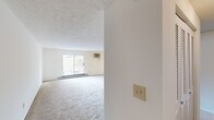 This single-story home offers a functional and comfortable layout with five bedrooms, two bathrooms, a living room, and a kitchen, all connected by two hallways. The living room is bright and airy, featuring plush carpeting, a textured ceiling, a wall-mounted HVAC unit, and a sliding glass door that fills the space with natural light and provides outdoor access. The kitchen is well-equipped, showcasing rich wooden cabinetry, granite-style countertops, white appliances including a range and dishwasher, and a window with a pleasant wooded view. The generously sized primary bedroom includes carpeted floors, a ceiling fan, a wall unit, baseboard heating, and a window with outdoor views. Additional bedrooms are carpeted and bright, with some featuring closets with louvered doors. The two bathrooms are finished with white subway tile and granite-topped vanities with framed mirrors. Consistent carpeting throughout the living areas and bedrooms contributes to a cohesive, comfortable feel, while baseboard heating is present across multiple rooms. The overall layout is practical and well-organized, offering ample space for multiple occupants.