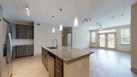This single-story, two-bedroom, two-bathroom residence offers a thoughtfully designed open-concept layout that seamlessly connects the kitchen, dining, and living areas. Light-toned wood-style flooring runs throughout the main living spaces, complementing the neutral color palette and contributing to a bright, cohesive atmosphere.

The kitchen serves as a central focal point, anchored by a large island with granite countertops and an undermount sink, illuminated by stylish pendant lighting. Dark wood cabinetry, a subway tile backsplash, stainless steel appliances—including a refrigerator, range, and dishwasher—and a dedicated in-unit washer and dryer complete this functional space. Track lighting adds additional illumination over the cooking area.

The living area is spacious and airy, featuring a ceiling fan and access to an outdoor balcony, allowing natural light to flow freely. Both bedrooms are carpeted, include ceiling fans, and feature windows with exterior views, creating comfortable, well-lit retreats.

Each bathroom is finished with large-format tile flooring and granite-topped dark wood vanities. The primary bathroom includes a soaking tub, separate shower, and a generously sized walk-in closet with built-in wire shelving. The second bathroom features a dual-sink vanity for added convenience.