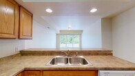 Located at 215 W Cascade Ave in River Falls, Wisconsin, this single-floor, 4-bedroom, 2-bathroom home offers a well-organized and functional layout. The kitchen is a standout feature, outfitted with warm wood cabinetry, laminate countertops, a double stainless steel sink, and white appliances including a range, microwave, refrigerator, and dishwasher. Light wood-style flooring runs throughout the main living areas and bedrooms, lending a clean and cohesive look to the space. The hallway connects the rooms efficiently, with dark wood-framed doors adding a touch of contrast against the neutral walls. The primary bedroom is generously sized and includes a built-in desk or countertop surface along with a closet area, offering added convenience. The two bathrooms are finished with tile flooring and full tub-shower combinations. A dedicated laundry room houses a full-size washer and dryer alongside the water heater and utility systems, keeping essentials neatly contained. Natural light filters in through windows, including a kitchen window with views of surrounding greenery. The overall design is clean, practical, and well-maintained, making this home a solid and comfortable option in the River Falls community.