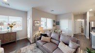 This single-floor residence offers a thoughtfully designed layout with a contemporary aesthetic carried consistently throughout each space. The kitchen serves as a functional centerpiece, featuring flat-front cabinetry in a warm taupe finish, stainless steel appliances including a gas range, built-in microwave, and French door refrigerator. A large island with a white quartz countertop provides bar seating, illuminated by pendant lighting overhead. Dark hardwood-style flooring runs through the kitchen and living areas, grounding the neutral color palette.

The open living room receives generous natural light through multiple windows dressed with horizontal blinds, offering views of the surrounding neighborhood. The space comfortably accommodates a full sectional and additional seating, creating a welcoming, versatile area.

The primary bedroom is notably well-lit, with wide windows along one wall and soft carpet underfoot. A second bedroom mirrors this bright, calm atmosphere. Both rooms feature neutral wall tones and ample space for furnishings.

The bathroom includes large-format tile flooring, a wood-toned vanity with white countertop, a wall-mounted toilet, and a glass-enclosed walk-in shower, delivering a clean, modern finish throughout.
