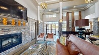 Located at 11100 Beckstone Way in Raleigh, NC, this expansive single-story community clubhouse offers a generously sized, amenity-rich layout designed for both relaxation and entertainment. The grand entrance greets visitors with soaring two-story ceilings, stacked-stone columns, and large glass double doors that flood the space with natural light and offer views of the surrounding landscaping.

The open-concept main area features polished concrete floors, coffered ceilings with elegant pendant lighting, and stacked-stone accent walls that lend a warm, upscale-rustic character throughout. A fully equipped kitchen showcases dark cabinetry, granite countertops with a stone-clad island, mosaic tile backsplash, stainless steel appliances, and pendant lighting — ideal for hosting events and gatherings.

Adjacent to the kitchen, a spacious game and dining area includes a billiards table, shuffleboard, and high-top seating with distinctive cowhide-print chairs, all framed by large windows with rich drapery. The lounge area provides comfortable leather seating arranged around a fireplace and wall-mounted television.

A dedicated theater room offers tiered seating with plush armchairs, a large projection screen, decorative wall sconces, and tailored Art Deco-inspired molding details, creating an immersive cinematic experience. Together, these spaces form a cohesive, well-appointed clubhouse designed for community living at its finest.