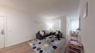 This well-designed single-floor residence offers a comfortable and functional layout with multiple bedrooms, two full bathrooms, a shared living area, and a dedicated kitchen and dining space. The open living room features light wood-style flooring, white walls, and large windows fitted with roller shades that allow for ample natural light. A sectional sofa and a colorful polka-dot area rug anchor the space, which flows seamlessly into the dining area with bar-height seating. The galley-style kitchen is equipped with granite-look countertops, white cabinetry with gold hardware, a double-basin sink, and a full-size refrigerator, with views into the adjacent dining nook. Each bedroom offers a distinct character while maintaining a cohesive, clean aesthetic. Ceiling fans, wood-style flooring, and generous window placement are consistent throughout the bedrooms, providing good ventilation and natural light. One bedroom features a dedicated study desk, making it well-suited for a student or remote worker. Both bathrooms include a full tub-shower combination with white tile surround and wood-style flooring. Overall, the residence presents a bright, neutral palette with a warm and livable ambiance throughout.