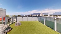 Located at 1770 Pendrell St in Vancouver's West End, this rooftop terrace offers a thoughtfully designed outdoor space with breathtaking panoramic views. The terrace is divided into distinct zones, each serving a different purpose while sharing the same spectacular backdrop of English Bay, the North Shore mountains, and the Vancouver city skyline.

The space features a generous artificial turf lawn area adorned with natural boulder accents, providing a relaxed, park-like setting. Glass panel railings line the perimeter throughout, ensuring unobstructed sightlines across the water and cityscape. A dedicated lounging area with striking red sculptural chaise lounges is positioned against an exposed concrete architectural element, creating a bold visual contrast.

A social and dining zone features red picnic-style tables surrounded by large steel planters filled with lush greenery and herbs, adding a living, organic element to the rooftop. Tiled paving in neutral tones connects the various areas seamlessly, while sections of decorative gravel provide low-maintenance landscaping detail. Horizontal louvered architectural screens on the building's mechanical structures add a refined industrial aesthetic. The terrace receives abundant natural light throughout the day, making it an ideal space for relaxation, social gatherings, and taking in Vancouver's iconic outdoor scenery.