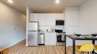This thoughtfully designed single-floor unit offers a functional and modern layout across several distinct living areas. The kitchen is outfitted with stainless steel appliances, including a full-size refrigerator, dishwasher, electric range, and over-the-range microwave. Crisp white cabinetry extends to the ceiling, providing generous storage, while a subway tile backsplash and light countertops add a clean, contemporary aesthetic. Light wood-tone flooring runs throughout, lending warmth and continuity to the space. Adjacent to the kitchen, a compact dining area accommodates a bistro-style table and benefits from a window that draws in natural light, creating a bright and welcoming atmosphere. The living area features a corner window that fills the room with daylight and offers views to the outside, providing an airy, open feel. The bedroom is a well-proportioned retreat with a dedicated walk-in closet, soft neutral walls, and continued wood-tone flooring. The full bathroom is finished in clean white tile and includes a shower with a curved curtain rod, toilet, and an efficiently arranged layout. Recessed lighting throughout the unit enhances the modern, polished character of the space.
