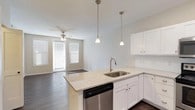 This single-story residence offers a well-designed, open layout that seamlessly connects the kitchen and living areas. The kitchen is a standout feature, equipped with crisp white shaker-style cabinetry, light granite countertops, and a full suite of stainless steel appliances, including a range, over-the-range microwave, dishwasher, and refrigerator. A peninsula island with an undermount sink provides additional prep space and serves as a natural transition into the living area, which is illuminated by natural light through blinds-fitted windows and complemented by a ceiling fan overhead. Dark hardwood-style flooring runs throughout the main living and kitchen spaces, adding warmth and contrast to the light color palette.

The bedroom is a comfortable, carpeted retreat featuring a ceiling fan, neutral walls, and a pair of windows that bring in ample natural light. The bathroom is thoughtfully appointed with a dual-sink vanity topped with granite counters, a large mirror, and a tiled walk-in shower. An adjacent walk-in closet provides generous storage. Throughout the space, consistent finishes—brushed nickel hardware, neutral tones, and quality materials—create a cohesive and functional living environment.