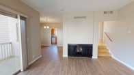 This two-story home offers a well-organized layout with distinct living spaces across both levels. The main living area is anchored by a striking floor-to-ceiling white wood-paneled fireplace with a black surround, serving as a central focal point. Durable hardwood-style flooring flows throughout the main level, complemented by neutral beige walls and a textured ceiling. A sliding glass door connects the living room to an outdoor balcony, allowing natural light to fill the space. A chandelier-lit dining area transitions seamlessly toward the kitchen, which features warm wood cabinetry, granite-style countertops, a gas range, and a window overlooking the exterior.

The upper level houses multiple bedrooms finished with plush carpeting and standard textured ceilings. Each bedroom benefits from natural light through horizontal sliding windows. The primary bedroom includes a built-in closet with shelving, an additional reach-in closet, and direct access to a private bathroom. A separate bathroom features a clean, white tub-shower enclosure. Additional rooms provide flexible space suitable for various needs, with easy access to hallways finished in warm parquet-style flooring.