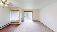 This single-floor unit offers a practical and straightforward layout designed for comfortable everyday living. The kitchen is efficiently arranged with rich, dark wood cabinetry, granite-toned countertops, and stainless steel appliances including a gas range, microwave, and refrigerator. Hardwood-style flooring runs through the kitchen and adjoining dining area, creating a clean transition into the carpeted living spaces. A ceiling fan fixture adds functionality to the dining area.

The living room is generously sized, featuring plush carpeting, neutral walls, and a sliding glass door dressed with vertical blinds that opens to an outdoor view of surrounding greenery. Baseboard heating units are present throughout, ensuring consistent warmth across all rooms. A second carpeted bedroom also features a sliding glass door with tree-lined views, while an additional bedroom benefits from a large window that invites natural light and outdoor scenery.

The bathroom is clean and well-appointed, featuring a full soaking tub with a tiled surround, a wall-mounted sink, a large mirror, and a chrome three-bulb vanity light fixture. Overall, the unit maintains a bright, neutral palette throughout, creating a calm and functional living environment.
