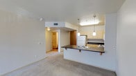 Located at 453 13th Street in the heart of San Diego, CA, unit 407 is a single-floor residence that combines functional design with a comfortable living environment. The open-concept layout connects the living area to the kitchen, creating a seamless flow throughout the main living space. Soft, neutral-toned carpet runs throughout, lending a warm and cohesive feel to the interior.

The kitchen is a standout feature, equipped with light wood cabinetry, a dark countertop peninsula with a double sink and breakfast bar seating, and pendant lighting that adds a modern touch overhead. A white refrigerator and range complete the kitchen setup, while the peninsula provides a natural divider between the kitchen and the open living area.

Adjacent to the main living space, a hallway leads to additional rooms, including what appears to be a carpeted bedroom with clean, neutral walls offering a blank canvas for personalization. A closet area is accessible nearby, providing practical storage solutions.

Throughout the unit, the color palette remains light and airy, with white walls and ceilings that help maximize the sense of space. Recessed HVAC vents and consistent lighting fixtures contribute to a tidy, well-maintained interior. This unit offers a straightforward and livable layout in a convenient San Diego location.