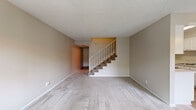 This two-story residence offers a practical and well-organized layout, with living space evenly distributed across both floors. The main level features a spacious carpeted living area with neutral-toned walls and a textured ceiling, anchored by a staircase with a white railing that leads to the upper floor. The galley-style kitchen is a functional highlight, featuring white cabinetry on both sides, light quartz-style countertops, wood-look flooring, stainless steel appliances including a refrigerator and electric range, and a built-in sink with an adjacent dishwasher. The bathroom is finished with wood-look flooring, a white vanity with storage, and a full tub-shower combination with a sliding glass enclosure and a small window for ventilation. Upstairs, the three bedrooms are carpeted and bathed in natural light from generously sized windows, with views of surrounding greenery. The spacious primary bedroom features mirrored sliding closet doors, adding a sense of depth to the room. Additional bedrooms are well-proportioned and versatile. Multiple hallways provide logical flow throughout the home, and a dedicated closet offers supplemental storage. Textured ceilings are consistent throughout the residence.