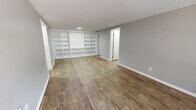 Located at 2100 Apalachee Parkway in Tallahassee, Florida, this 2-bedroom, 2-bathroom unit offers a practical and well-organized single-floor layout. The combined living and dining area serves as the centerpiece of the home, featuring warm wood-look flooring, neutral gray walls, a textured ceiling, and a striking wall of built-in white shelving — ideal for display or storage. Natural light filters in through a window framing views of the surrounding greenery. The kitchen is equipped with white cabinetry, dark granite-style countertops, and an electric range with overhead ventilation. Both bathrooms mirror each other in design, each offering wood-look tile flooring, a tub-shower combo, a white vanity with dark countertop, and built-in shelving. The primary bedroom features carpeted flooring, a ceiling fan, a window with exterior views, and a built-in bench beneath the window. The second bedroom also offers carpet, soft neutral tones, and a spacious double-door closet. With six closets total and a dedicated laundry area, this unit provides ample storage throughout. The consistent neutral palette and cohesive finishes give the space a clean, functional character well-suited for everyday living.
