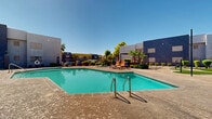 Located at 1333 N Dysart Rd in Avondale, Arizona, this outdoor community amenity space is designed to offer residents a comprehensive recreational environment under the abundant Arizona sun. At the heart of the space is a generously sized swimming pool with striking turquoise water, accented by classic blue diamond tile details and surrounded by a spacious concrete pool deck. Poolside loungers and a shaded pergola-style cabana provide comfortable spots to relax, while tall palm trees and mature shade trees add a resort-like atmosphere.

Adjacent to the pool area, a covered pergola structure strung with globe lighting serves as a dedicated outdoor dining and gathering space, furnished with multiple blue picnic-style tables — ideal for community events or casual meals. Nearby, a putting green with artificial turf offers a leisure activity option for residents.

The grounds are enclosed by ornamental iron fencing and gates, providing a secure, well-defined perimeter. Landscaping throughout features desert-adapted shrubs, ground cover, and decorative rock mulch that complement the Southwest setting. Outdoor seating vignettes with patio chairs and market umbrellas are strategically placed throughout, creating inviting social areas. The overall ambiance is vibrant and community-oriented, with a clean, modern aesthetic reinforced by the bold color accents of the surrounding buildings.