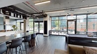 Located on the third floor of 51 E 14th Street in Chicago's South Loop, this modern amenity floor delivers a well-rounded communal experience through a series of thoughtfully designed spaces. The open-concept main area features exposed concrete ceilings with industrial-style ductwork and black pendant linear lighting, creating a contemporary urban aesthetic. Wide-plank flooring runs throughout, anchoring the various activity zones beneath soaring ceilings.

The social lounge offers plush seating arranged around a sleek linear fireplace and a large wall-mounted television, perfect for gathering and relaxing. Floor-to-ceiling windows bathe the space in natural light and frame views of the surrounding Chicago cityscape, with direct access to an outdoor terrace furnished for al fresco dining and lounging.

A fully equipped demonstration kitchen anchors the entertaining area, complete with a large island, stainless steel appliances, an induction cooktop, and a professional range hood. High-top communal tables and bar seating provide additional space for dining and socializing, while a billiards table adds a recreational element to the open lounge.

A private conference room with a rich wood table and tan leather chairs offers a quieter setting for meetings, accented by curated wall art. Restrooms and a water station round out the practical amenities, ensuring this floor is fully equipped for both work and leisure.