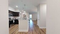 Located at 1000 Revere Place in Spring Hill, Tennessee, this well-appointed 2-bedroom, 1-bathroom single-floor home offers a thoughtfully designed layout with modern finishes throughout. The open-concept living area is anchored by warm hardwood-style flooring and flows seamlessly from the living room to the dining area and kitchen. The living room features a glass-panel exterior door flanked by large windows, filling the space with natural light. A cozy dining nook sits adjacent to the kitchen, offering an intimate setting for meals. The kitchen is a standout, boasting dark cabinetry with a white subway tile backsplash, granite countertops, stainless steel appliances, and a peninsula with bar seating illuminated by stylish pendant lights. The spacious primary bedroom features plush carpet, a ceiling fan, and a large window with outdoor views, along with access to a generous walk-in closet with wire shelving. The second bedroom is equally comfortable with soft carpet flooring. The full bathroom includes a dark vanity with a white countertop, tile flooring, and a tub-shower combination. A dedicated laundry room with side-by-side washer and dryer hookups and built-in shelving adds everyday convenience to this move-in-ready home.