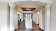 This two-story home in Toledo, Ohio offers three bedrooms, three bathrooms, and a thoughtfully designed layout spread across two floors. The main level makes an immediate impression with its open-concept kitchen, framed by a striking arched entryway and anchored by a standout wood-planked tray ceiling with track lighting. The kitchen features white cabinetry, stainless steel appliances including a refrigerator, range, and microwave, light stone countertops, and a center island with a double sink — ideal for both cooking and entertaining. The living room receives generous natural light through large windows and a glass-paneled door, creating a bright and welcoming atmosphere with neutral-toned carpet. The upper floor hosts the spacious primary bedroom, distinguished by vaulted ceilings and a large closet, providing a comfortable and airy retreat. Additional bedrooms are carpeted and well-lit, with windows offering outdoor views. Three full bathrooms are distributed across both floors, each featuring tub-shower combinations with white tile surrounds. Two closets provide practical storage, while a hallway and staircase connect the floors seamlessly. Neutral gray walls and dark hardwood flooring on the main level give the home a clean, cohesive aesthetic throughout.