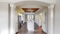 This two-story home in Toledo, Ohio offers three bedrooms, three bathrooms, and a thoughtfully designed layout spread across two floors. The main level makes an immediate impression with its open-concept kitchen, framed by a striking arched entryway and anchored by a standout wood-planked tray ceiling with track lighting. The kitchen features white cabinetry, stainless steel appliances including a refrigerator, range, and microwave, light stone countertops, and a center island with a double sink — ideal for both cooking and entertaining. The living room receives generous natural light through large windows and a glass-paneled door, creating a bright and welcoming atmosphere with neutral-toned carpet. The upper floor hosts the spacious primary bedroom, distinguished by vaulted ceilings and a large closet, providing a comfortable and airy retreat. Additional bedrooms are carpeted and well-lit, with windows offering outdoor views. Three full bathrooms are distributed across both floors, each featuring tub-shower combinations with white tile surrounds. Two closets provide practical storage, while a hallway and staircase connect the floors seamlessly. Neutral gray walls and dark hardwood flooring on the main level give the home a clean, cohesive aesthetic throughout.