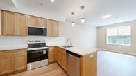 Located at 1550 Empire Blvd in Webster, NY, this 2-bedroom, 1-bathroom residence offers a thoughtfully designed single-floor layout with modern finishes throughout. Light-toned luxury vinyl plank flooring runs through the main living areas, complemented by neutral warm beige walls and crisp white trim that create a clean, cohesive aesthetic.

The kitchen is a standout feature, showcasing natural wood-toned shaker cabinetry, white quartz countertops, a classic subway tile backsplash, and a full suite of stainless steel appliances including a range, microwave, dishwasher, and refrigerator. A peninsula with an integrated double sink and pendant lighting above adds both function and style, opening seamlessly to the combined dining and living area.

A connecting hallway leads to two well-sized bedrooms, both carpeted in neutral tones for comfort. The primary bedroom is generously proportioned and features multiple windows that invite abundant natural light and outdoor views. The second bedroom offers a quiet, versatile space. Four closets throughout the unit provide ample storage.

The layout is completed by a full bathroom and a hallway connecting the private and shared spaces efficiently. Overall, the residence presents a modern, move-in-ready environment with a clean, functional design suited for everyday living.