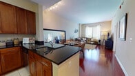 Located at 1910 Towne Centre Blvd in Annapolis, Maryland, this well-appointed single-floor residence offers a thoughtfully designed open-concept layout that seamlessly connects the kitchen, dining, and living areas. Rich hardwood flooring flows throughout the main living spaces, creating a warm and cohesive aesthetic.

The kitchen is a standout feature, outfitted with warm cherry wood cabinetry, dark granite countertops, stainless steel appliances — including a range, microwave, and dishwasher — and a peninsula with an integrated sink that opens directly to the dining and living areas. Light tile flooring anchors the kitchen zone, providing a clean contrast to the surrounding hardwood.

The living room is generously sized, bathed in natural light through large windows with outdoor views, and offers ample space for comfortable seating arrangements. The bedroom continues the hardwood flooring theme and features large windows that fill the room with natural light and provide expansive views of the surrounding area, adding a bright and airy quality to the space.

The bathroom is finished with tile flooring, a white vanity with storage, and a full tub-shower combination. The overall color palette is neutral and understated, with warm tones throughout, contributing to a calm and inviting atmosphere across the entire residence.