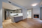 Located at 312 N Cayuga St in Ithaca, NY, this thoughtfully designed 2-bedroom, 2-bathroom residence offers a clean, modern aesthetic across a well-organized single-floor layout. The living room serves as the heart of the home, featuring warm hardwood flooring, crown molding, a sleek built-in fireplace, and multiple windows that invite abundant natural light and views of the surrounding neighborhood. The kitchen is well-appointed with shaker-style cabinetry in a soft gray finish, white quartz countertops, stainless steel appliances including a range with overhead hood and built-in microwave, and under-cabinet lighting — all set on light hardwood floors. Both bedrooms are carpeted in a neutral tone and bathed in natural light from generously sized windows. The spacious primary bedroom offers a comfortable, quiet retreat, while the second bedroom benefits from dual windows with views of the streetscape. The two bathrooms are finished with white subway tile walk-in showers, light tile flooring, and brushed nickel fixtures; one bathroom is equipped with accessibility features including grab bars and a fold-down shower bench. A connecting hallway ties all rooms together efficiently. This unit combines modern finishes with functional design in a prime Ithaca location.