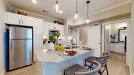 This well-designed single-floor residence offers a thoughtful layout that balances open communal living with comfortable private spaces. The heart of the home is a contemporary open-concept kitchen that flows seamlessly into the living area. Crisp white shaker-style cabinetry lines the kitchen walls, complemented by a classic subway tile backsplash, granite countertops, and a full suite of stainless steel appliances including a refrigerator with ice maker, built-in microwave, and range. A generously sized center island with a granite surface and integrated sink serves as both a functional workspace and a natural gathering point, illuminated from above by a trio of stylish pendant lights. Crown molding adds an elegant finishing touch to the kitchen and living areas, while warm-toned hardwood-style flooring runs throughout the main spaces.

The bedrooms are carpeted for comfort and filled with natural light through multiple windows fitted with blinds. Ceiling fans in each bedroom provide year-round climate control. The bathroom is finished with granite countertops, white cabinetry with matte black hardware, and hardwood-style flooring. It features a tiled soaking tub and shower combination, along with convenient access to a spacious walk-in closet. Throughout the home, a neutral color palette and clean architectural lines create a bright, modern, and welcoming atmosphere.