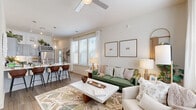 This well-appointed two-story home in North Charleston, SC offers a thoughtful layout across two floors. The main level hosts an open-concept kitchen and living area filled with natural light from large, plantation-shuttered windows. The kitchen stands out with powder-blue shaker cabinets, white quartz countertops, a subway tile backsplash, stainless steel appliances, and a built-in wine rack — a functional yet stylish space for cooking and entertaining. The adjacent living room features wood-look flooring, a ceiling fan, and a seamless flow that makes the space feel open and airy. A dedicated laundry room with a full-size washer and dryer adds everyday convenience. A staircase with wood-tread steps connects the main level to the upper floor, where both bedrooms are located. The spacious primary bedroom includes a ceiling fan, generous natural light, and ample room to furnish comfortably. The second bedroom is cozy and well-lit, with a large window offering outdoor views. Both bathrooms are finished with gray shaker vanities, white countertops, and wood-look tile flooring, with one featuring a full tub-shower combination. Throughout the home, a neutral palette and consistent hardwood-style flooring create a cohesive, modern aesthetic.