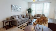 This single-floor residence at 549 Avenida Sexta in Clermont, Florida, offers a well-appointed layout designed for comfortable everyday living. The open living area is bright and welcoming, featuring large windows dressed with sheer curtains and horizontal blinds that allow abundant natural light to fill the space. Plush carpeting, a ceiling fan with integrated lighting, and access to an exterior door contribute to the room's airy, relaxed atmosphere. The kitchen is efficiently designed with warm wood cabinetry, tile flooring, a full-size refrigerator, a range, and a built-in microwave, providing all the essentials in a compact, functional arrangement. The primary bedroom is generously sized, with carpeted floors, large windows with sheer drapery, and a private door leading to an outdoor area, adding a sense of openness to the room. A spacious walk-in closet with wire shelving offers ample storage. The bathroom is finished with tile-surround tub and shower combination, tile flooring, and clean, neutral fixtures. Throughout the residence, neutral wall tones and consistent finishes create a cohesive, move-in-ready environment suited to a variety of personal styles.