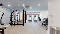 Located at 801 E Whiting St in Tampa, Florida, this fitness facility is thoughtfully designed across two dedicated exercise rooms, offering a comprehensive and well-organized workout environment. The space features a clean, modern aesthetic with crisp white and light gray walls, recessed lighting throughout, and durable flooring suited for high-traffic athletic use.

The primary exercise room is equipped with a robust lineup of cardio machines, including treadmills, ellipticals, and a stair climber, arranged along the perimeter to maximize open floor space. A power rack with a flat bench anchors the strength training area, while a wall-mounted mirror expands the sense of space and supports proper form during workouts. Ceiling-mounted HVAC units ensure climate comfort throughout.

The second exercise room provides a quieter, more versatile training environment. A full multi-function cable machine takes center stage, complemented by a rowing machine, wall-mounted flat-screen television, and additional strength machines. A full rack of dumbbells lines one wall, supported by a mirrored backdrop that enhances the open feel of the room.

Both rooms are connected by a corridor that houses additional isolated strength machines, making transitions between training areas seamless. The facility's neutral color palette, ample recessed lighting, and thoughtful equipment layout create a professional yet inviting atmosphere for a wide range of fitness routines.