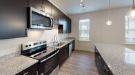 This single-floor residence offers a thoughtfully designed layout that balances functionality with contemporary style. The kitchen serves as a visual centerpiece, featuring dark espresso cabinetry, stainless steel appliances including a range, microwave, and refrigerator, and granite-style countertops. Wood-look flooring runs throughout the kitchen and main living areas, lending warmth and cohesion to the space.

The bedrooms are carpeted and finished in soft neutral tones, with multiple windows dressed in horizontal blinds that allow natural light to filter in. The primary bedroom connects to a spacious walk-in closet outfitted with wire shelving systems, offering generous storage capacity. An additional closet provides further organizational flexibility.

The bathrooms are clean and functional, each featuring a tub-shower combination with white tile surrounds. The primary bathroom includes a long vanity with dark cabinetry, granite-style countertops, and wood-look flooring, creating a cohesive aesthetic that mirrors the kitchen design.

A hallway connects the living areas to the bedrooms, maintaining a logical and efficient flow throughout the unit. Overall, the space presents a modern, move-in-ready environment with consistent finishes and ample natural light.