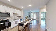 Located in Mauldin, South Carolina, this well-designed one-bedroom, one-bathroom residence offers a smart, functional layout across a single floor. The open-concept kitchen and living area serves as the heart of the home, featuring crisp white cabinetry, a subway tile backsplash, granite-style countertops, and a full suite of stainless steel appliances including a refrigerator, range, and microwave. Recessed lighting and light wood-look flooring run throughout, creating a clean, contemporary aesthetic. The living area extends naturally toward a private door and windows that invite abundant natural light and provide outdoor access. The bedroom is a comfortable, well-proportioned retreat with neutral-toned walls, a ceiling fan, large windows overlooking greenery, and direct access to a dedicated walk-in closet. The bathroom is finished with a white vanity, granite countertop, a large framed mirror, and hardwood-style flooring that ties the space together cohesively. A separate utility room provides practical storage and housing for mechanical systems. Throughout the residence, consistent use of light tones, modern hardware, and wood-look flooring creates a cohesive, move-in-ready environment ideal for those seeking a streamlined and efficient living space.