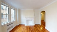 This single-floor residence showcases a blend of traditional architectural character and functional design. Rich hardwood floors run continuously throughout, lending warmth and cohesion to every room. The living room serves as a focal point, highlighted by a stately white decorative fireplace with an ornate mantel and chimney surround, crown molding, and natural light from double-hung windows. An elegant arched doorway connects the living area to the rest of the unit, adding a refined architectural detail that carries through the hallway.

The bedroom offers a quiet retreat with its own window overlooking the exterior, complemented by hardwood floors and a generous walk-in closet fitted with built-in shelving. A secondary room provides flexible space, also featuring hardwood flooring and clean, neutral walls.

The kitchen is compact and efficiently laid out, equipped with a gas range, stainless steel sink, dishwasher, white cabinetry with wood trim, white countertops, and a classic tile floor. A window above the sink provides natural light. The bathroom maintains a timeless aesthetic with white subway-style wall tile, a classic black-and-white basket-weave tile floor, a pedestal-style vanity, and a window for ventilation and light.