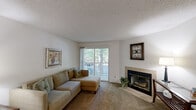 This well-appointed single-floor residence offers a functional and comfortable layout across several distinct living areas. The living room serves as the heart of the home, featuring a tiled wood-burning fireplace, plush wall-to-wall carpeting, and a sliding glass door that opens onto a private balcony with views of mature surrounding trees, allowing natural light to fill the space.

The galley-style kitchen is equipped with rich wood cabinetry, granite-look countertops, a double-basin sink, and white appliances including an electric range and refrigerator. Wood-look flooring adds warmth to this functional cooking space, which connects directly to the laundry room.

The dedicated laundry room includes a full-size washer and dryer set, wire shelving for additional storage, and wood-look flooring—providing convenient in-unit utility.

The space includes two bedrooms, both finished with soft carpeting and textured ceilings. The primary bedroom is generously sized, offering ample room for large furnishings and featuring a window that invites natural light. The secondary bedroom is equally comfortable, with a window and cozy, intimate atmosphere.

Throughout the residence, a consistent neutral color palette, textured ceilings, and carpeted floors create a cohesive and understated aesthetic well-suited for everyday living.