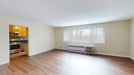Located at 8600 Skokie Blvd in Skokie, Illinois, this single-floor unit offers a clean, functional layout with a neutral color palette and consistent hardwood-style flooring throughout. The spacious living area is bright and open, featuring large windows with vertical blinds that allow generous natural light to fill the room, along with a built-in PTAC heating and cooling unit beneath the window. The bedroom is generously sized, benefiting from dual windows on adjacent walls that further enhance natural light, and includes sliding mirrored closet doors providing ample storage space. The galley-style kitchen is well-appointed with light maple cabinetry, dark granite countertops, a mosaic tile backsplash, and stainless steel appliances including a dishwasher. A window at the end of the kitchen adds additional brightness to the space. The bathroom features classic black-and-white octagonal tile flooring, white subway tile surrounding the shower-tub combination, a white vanity with storage, and a natural light source via a sliding window. Throughout the unit, crisp white trim and warm beige walls contribute to a tidy, move-in ready ambiance.