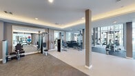 Located at 1614 N Congress Ave in West Palm Beach, Florida, this expansive fitness center spans a generously sized single floor designed to accommodate a comprehensive range of workout activities. The space is thoughtfully organized into distinct zones, each tailored to specific training disciplines, while maintaining an open, cohesive layout throughout.

The strength training area features an extensive array of cable machines, selectorized weight equipment, a power rack, and a full dumbbell rack, all set against large wall-mounted mirrors that visually expand the space. Recessed lighting combined with an illuminated tray ceiling creates a polished, well-lit environment. Flooring transitions between textured carpet tiles and smooth hard surfaces, delineating training zones naturally.

A dedicated cardio section houses treadmills and rowing machines, positioned near floor-to-ceiling windows that invite natural light and offer views of the surrounding West Palm Beach landscape. Decorative pendant lighting in warm amber tones adds an upscale aesthetic accent.

A separate cycling studio features light wood-tone flooring, white structural columns, and glass partition walls with direct outdoor access, contributing to an airy, open ambiance. Built-in shelving and louvered storage doors provide practical organization. Throughout, the design balances functionality with contemporary style, making this a well-appointed, professional-grade fitness facility.