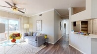 This well-appointed 2-bedroom, 2-bathroom single-story residence offers a thoughtfully designed open layout that maximizes functionality and comfort. The living room features hardwood-style flooring, crown molding, a ceiling fan, and a sliding glass door that invites natural light and outdoor views. Adjacent to the living area, the dining space is defined by its open connection to the kitchen via a pass-through counter, creating a seamless flow ideal for entertaining. The kitchen is equipped with rich dark wood cabinetry, stainless steel appliances including an electric range and over-the-range microwave, a decorative tile backsplash, and white countertops. The primary bedroom offers plush carpeting and its own en-suite bathroom featuring a single vanity with white countertops and dark cabinetry. The second bedroom, painted in a distinctive teal tone, benefits from abundant natural light through multiple windows with sheer curtains. A second full bathroom includes a tiled shower-tub combination with sliding glass doors and wood-style flooring. A hallway connecting the main living areas also provides access to in-unit washer and dryer hookups. A dedicated closet adds practical storage to complete this efficiently organized residence.