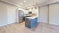 Located at 2001 Benvoulin Court in Kelowna, BC, this modern one-bedroom, one-bathroom unit offers a thoughtfully designed open-concept layout with contemporary finishes throughout. Light wood-tone flooring runs continuously across the living spaces, complementing the neutral palette and creating a bright, cohesive feel.

The kitchen is a standout feature, boasting a bold two-tone peninsula with a vivid blue gloss finish contrasted by crisp white upper cabinetry. A white quartz countertop, decorative pendant lighting, and a full suite of stainless steel appliances — including a French door refrigerator, microwave, and dishwasher — complete this well-appointed space. A stylish sliding barn door adds a modern architectural touch near the entryway.

The open living area extends toward a balcony with outdoor views, while a wall-mounted mini-split unit provides efficient climate control. The bedroom features a tray ceiling detail, a large window with natural light, a built-in sliding-door closet, and a baseboard heater. The full bathroom is clean and functional, offering a soaker tub/shower combo, grey-toned vanity with white countertop, and neutral tile flooring. A dedicated in-unit laundry area with full-sized washer and dryer adds everyday convenience to this well-designed Kelowna residence.