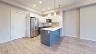 Located at 2001 Benvoulin Court in Kelowna, BC, this modern one-bedroom, one-bathroom unit offers a thoughtfully designed open-concept layout with contemporary finishes throughout. Light wood-tone flooring runs continuously across the living spaces, complementing the neutral palette and creating a bright, cohesive feel.

The kitchen is a standout feature, boasting a bold two-tone peninsula with a vivid blue gloss finish contrasted by crisp white upper cabinetry. A white quartz countertop, decorative pendant lighting, and a full suite of stainless steel appliances — including a French door refrigerator, microwave, and dishwasher — complete this well-appointed space. A stylish sliding barn door adds a modern architectural touch near the entryway.

The open living area extends toward a balcony with outdoor views, while a wall-mounted mini-split unit provides efficient climate control. The bedroom features a tray ceiling detail, a large window with natural light, a built-in sliding-door closet, and a baseboard heater. The full bathroom is clean and functional, offering a soaker tub/shower combo, grey-toned vanity with white countertop, and neutral tile flooring. A dedicated in-unit laundry area with full-sized washer and dryer adds everyday convenience to this well-designed Kelowna residence.