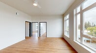 Located at 420 Center St NE in Salem, Oregon, this modern 2-bedroom, 1-bathroom unit offers a thoughtfully designed single-floor layout with clean contemporary aesthetics. Light hardwood flooring runs throughout, complementing the crisp white walls and black-trimmed doorframes that define the unit's modern character.

The open living area is bright and airy, benefiting from large multi-pane windows and a glass door that frame views of the surrounding cityscape. A ceiling fan adds both function and style to the space. The living area flows naturally toward the kitchen, which features warm wood cabinetry, white quartz countertops, a neutral tile backsplash, and black stainless appliances including a range, dishwasher, refrigerator, and over-range microwave.

Both bedrooms receive generous natural light through large windows overlooking the city. The primary bedroom includes a built-in closet with a sliding door. The bathroom offers a wide wood-tone vanity with white countertops, a large mirror, and coordinating black fixtures, maintaining the unit's consistent modern design language throughout.