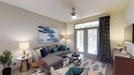 This single-floor residence is thoughtfully designed with a contemporary aesthetic, combining functionality and style throughout. The living area serves as a welcoming central space, featuring wood-style flooring, a ceiling fan, and large glass French doors that invite natural light and provide direct outdoor access. Neutral gray walls are accented by colorful artwork, and the open layout comfortably accommodates a sectional sofa and glass coffee table arrangement.

The kitchen is outfitted with dark espresso cabinetry extending to the ceiling for ample storage, light granite countertops, a tile backsplash, and a full suite of stainless steel appliances including a range, microwave, refrigerator, dishwasher, and a built-in wine cooler. Wood-style flooring continues throughout this space.

The bedroom is generously proportioned, with plush carpeting, a ceiling fan, and large windows that fill the room with natural light. A doorway connects directly to the bathroom, which features dark cabinetry with granite countertops, wood-style flooring, and a built-in open shelving unit offering convenient organizational storage. The overall color palette of teal, navy, and yellow accents gives the residence a cohesive, modern feel.