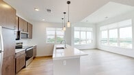 Located on Good Hope Road in Menomonee Falls, WI, this thoughtfully designed 2-bedroom, 2-bathroom single-floor residence offers a bright and contemporary living experience. The open-concept kitchen and living area serves as the heart of the home, featuring a large white quartz island with an integrated sink, warm wood cabinetry, stainless steel appliances, and stylish pendant lighting. Light hardwood flooring flows throughout the main living areas, complemented by large windows that flood the space with natural light and offer views of the surrounding landscape.

The living area extends seamlessly from the kitchen, making it ideal for both daily living and entertaining. A well-lit hallway connects the main living space to the private quarters. The generously sized primary bedroom is carpeted for comfort and includes a walk-in closet with built-in wire shelving. The second bedroom is equally well-appointed with carpet and its own closet access. Both bathrooms feature clean, modern finishes with wood-toned vanities and white countertops. A dedicated laundry room includes a stacked Whirlpool washer and dryer along with built-in wire shelving for added storage. The overall aesthetic is clean, modern, and move-in ready.