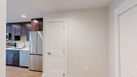 Located at 111 W Lamme St in the heart of Bozeman, Montana, this efficiently designed unit offers a thoughtful layout across a single floor, incorporating a kitchen, living room, bathroom, utility room, and closet. The open-concept kitchen and living area form the core of the space, featuring light hardwood-style flooring that runs throughout and recessed lighting overhead. The kitchen is outfitted with rich dark-stained wood cabinetry, white quartz countertops, a subway tile backsplash, and a full suite of stainless steel appliances including a refrigerator, range, microwave, and dishwasher. The living area benefits from multiple large windows that invite generous natural light and offer views of the surrounding Bozeman streetscape. Neutral, warm-toned walls complement the clean white trim and baseboards throughout. The bathroom is finished with a wood-toned vanity, white quartz countertop, an undermount sink, a large mirror, and a glass-enclosed walk-in shower. A dedicated utility room and closet provide practical storage and in-unit functionality. The overall aesthetic is modern and clean, presenting a well-appointed space well-suited for comfortable urban living in downtown Bozeman.