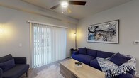 This single-floor unit is thoughtfully designed with a contemporary aesthetic and a neutral color palette that flows seamlessly from room to room. The living area serves as the heart of the space, featuring a ceiling fan, soft ambient lighting, and a large sliding glass door dressed with vertical blinds that allows generous natural light to fill the room. An adjacent dining area continues the modern sensibility with wood-look flooring, a pendant chandelier, and ample wall space.

The kitchen is equipped with stainless steel appliances — including a refrigerator, range, and over-the-range microwave — complemented by crisp white cabinetry and light quartz-style countertops, all set atop durable wood-look flooring. A versatile flex room, ideal as a home office or secondary bedroom, features plush carpeting, a ceiling fan, and a window with natural light. The bedroom area includes multiple closets with louvered bifold doors, providing practical storage.

Two full bathrooms mirror each other in design, each featuring wide white vanities with dual sinks, quartz-style countertops, and large mirrors. An in-unit laundry closet with wire shelving accommodates a full-sized washer and dryer, adding everyday convenience.