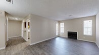 This single-floor, one-bedroom, one-bathroom residence offers a thoughtfully designed layout that maximizes comfort and functionality. The spacious living room is a standout feature, boasting wood-look hard flooring, neutral warm-toned walls, a textured ceiling, and multiple windows that flood the space with natural light. A classic fireplace anchors the room, adding a cozy focal point. The kitchen is well-equipped with rich dark wood cabinetry, light stone countertops, a tile backsplash, a stainless steel sink, and an adjacent pass-through window that connects to the laundry area — a convenient and practical touch. The dedicated laundry room houses a full-size washer and dryer set with overhead wire shelving for added storage. The bedroom is carpeted for comfort and features a ceiling fan with light fixture, a large window for natural light, and direct access to a spacious walk-in closet outfitted with dual wire shelving systems. The bathroom includes a full tub-shower combination with tiled surround, a toilet, vanity, and a small window for ventilation. Throughout, clean white trim, consistent neutral tones, and practical finishes create a cohesive and inviting living environment.