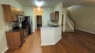 This two-story home in Grand Prairie, Texas offers a well-designed layout that connects living and functional spaces across both floors. The main level showcases warm hardwood-style flooring that extends throughout, creating a cohesive and inviting atmosphere.

The kitchen is a central highlight, featuring a peninsula with a dark granite countertop that doubles as a breakfast bar. Medium-toned cabinetry provides ample storage, complemented by a tile backsplash that adds texture to the space. Stainless steel appliances, including a refrigerator, range, and microwave, are built into the layout for a streamlined look. A walk-in pantry is conveniently accessible just off the kitchen, offering generous storage space.

The open sightlines from the kitchen toward the staircase give the main level a spacious, connected feel. The staircase, featuring a white balustrade and carpeted treads, leads to the second floor, where additional living space awaits. Light green walls on the main level contribute to a calm, neutral ambiance throughout the home.