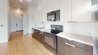 This contemporary single-floor unit showcases a clean, modern design throughout, unified by warm light wood flooring and crisp white walls that create a bright, airy atmosphere. The open-concept living area is generously proportioned, with large floor-to-ceiling windows that frame sweeping city and skyline views, flooding the space with natural light.

The kitchen is thoughtfully designed with a sleek two-tone aesthetic, featuring dark lower cabinetry paired with white upper cabinets and white quartz countertops. A full suite of stainless steel appliances — including a refrigerator, electric range, built-in microwave, and dishwasher — provides a fully equipped cooking environment.

The bedrooms are well-sized, each maintaining the consistent light wood flooring and white wall palette. One bedroom benefits from a large window with expansive outdoor views, while ample closet space is available, including a generous walk-in closet fitted with dual hanging rods and shelving.

The bathrooms are finished with white subway-style tile surrounding a soaking tub and shower, complemented by a floating vanity with a taupe countertop, undermount sink, and a large wall mirror. Consistent wood-look flooring extends into these spaces, maintaining a cohesive design language throughout the entire unit.