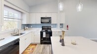Located at 109 Club Dr in Morganton, NC, this single-story, 3-bedroom, 2-bathroom home offers a clean, modern aesthetic throughout. Wood-look luxury vinyl plank flooring flows seamlessly across all rooms, complementing the neutral gray-toned walls and crisp white trim found throughout the space.

The kitchen is a standout feature, boasting tall white shaker cabinets, white quartz countertops, a light blue subway tile backsplash, and a bold blue center island topped with white quartz. Pendant lighting and black appliances, including a range, microwave, and refrigerator, complete this well-appointed space. The open layout connects easily to the hallway and living areas.

The spacious primary bedroom features vaulted ceilings with a skylight, a ceiling fan, and sliding glass doors that open to an outdoor deck with exterior views. The additional bedrooms are bright and well-proportioned, each with windows fitted with blinds and ceiling fans for comfort.

Both bathrooms are finished with white vanities, quartz countertops, framed mirrors, and stylish brushed nickel fixtures. One bathroom includes a window that brings in natural light. A connecting hallway links all rooms efficiently, keeping the single-floor layout practical and easy to navigate.